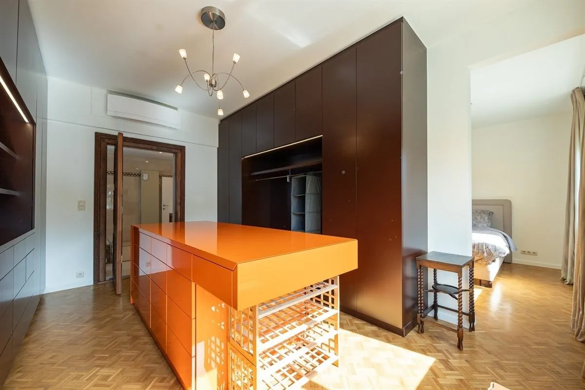 Dressing met donkere kastenwanden en een oranje eiland